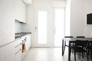 A modern kitchen with white cabinets, a stainless steel stove, and a dining area with a table and chairs.