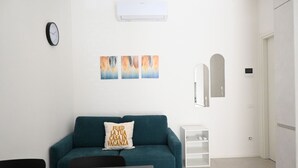 A modern living room with a teal sofa, a small white side table, a wall-mounted clock, and three abstract paintings. -  SE192 - Senigallia, new two-room apartment 50 meters from the sea (Senigallia)