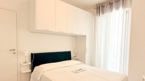 A hotel room with a bed, a nightstand, a lamp, a wardrobe, and a window with curtains. -  SE192 - Senigallia, new two-room apartment 50 meters from the sea (Senigallia)