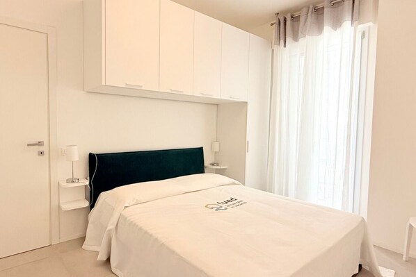 A hotel room with a bed, a nightstand, a lamp, a wardrobe, and a window with curtains.