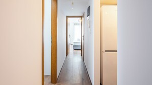 A narrow hallway with wooden flooring, a white wall, and a door leading to a bedroom. - Alex's 2-Bedroom Apartment in Athens (Athens)