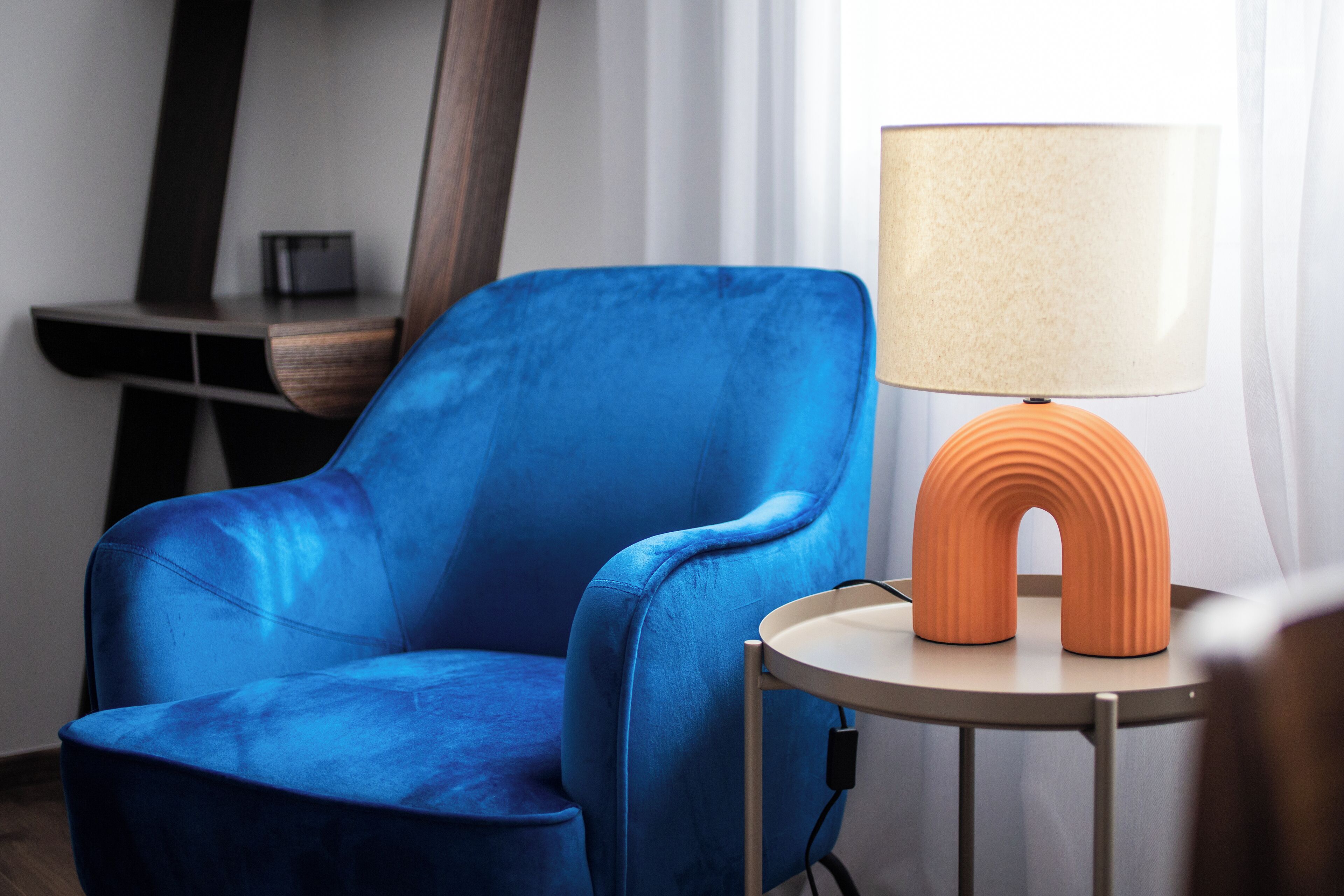 Un fauteuil bleu est placé à côté d’une table ronde sur laquelle se trouve une lampe.