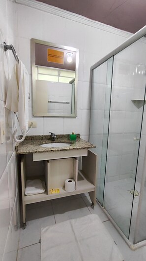 Baño con lavamanos de encimera de granito, espejo, cabina de ducha de vidrio y perchero.