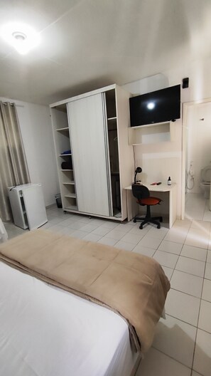 Una habitación de hotel con una cama, un escritorio con silla, un televisor y un armario.