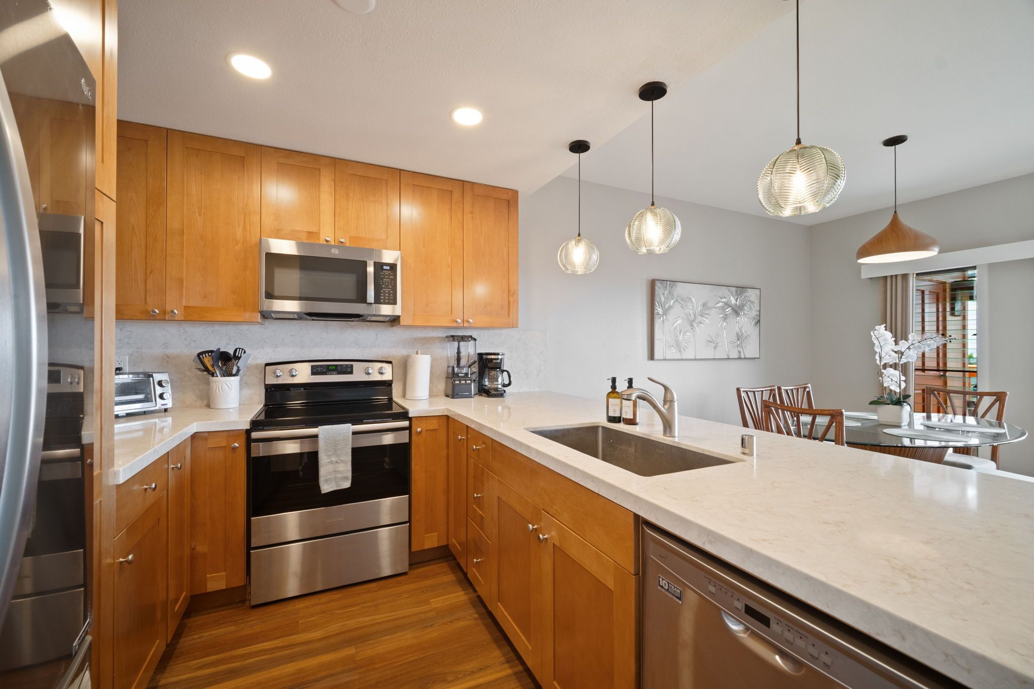 A modern kitchen with wooden cabinets, stainless steel appliances, a large island with a sink, and pendant lighting.