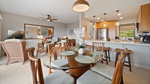 Cocina moderna con una isla central, comedor con sillas de mimbre y un espejo grande.