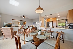 A modern kitchen with a central island, dining area with wicker chairs, and a large mirror. - Ocean View | 2 Pools | Spacious 3-Bed Makanui Condo in Poipu (Poipu)