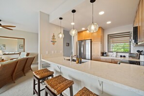 A modern kitchen with a large island, stainless steel appliances, and pendant lighting. - Ocean View | 2 Pools | Spacious 3-Bed Makanui Condo in Poipu (Poipu)