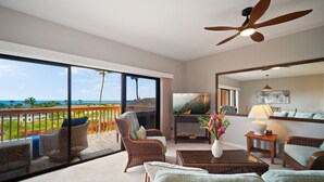 Una habitación amplia con un balcón grande, muebles de mimbre, televisión y ventilador de techo.