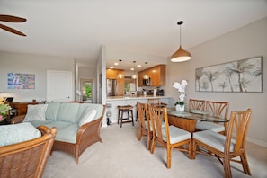 A living room with a sofa, dining table, chairs, and a kitchen in the background. - Ocean View | 2 Pools | Spacious 3-Bed Makanui Condo in Poipu (Poipu)