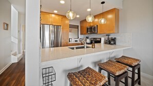 Una cocina moderna con armarios de madera, electrodomésticos de acero inoxidable, encimera de mármol y taburetes trenzados.