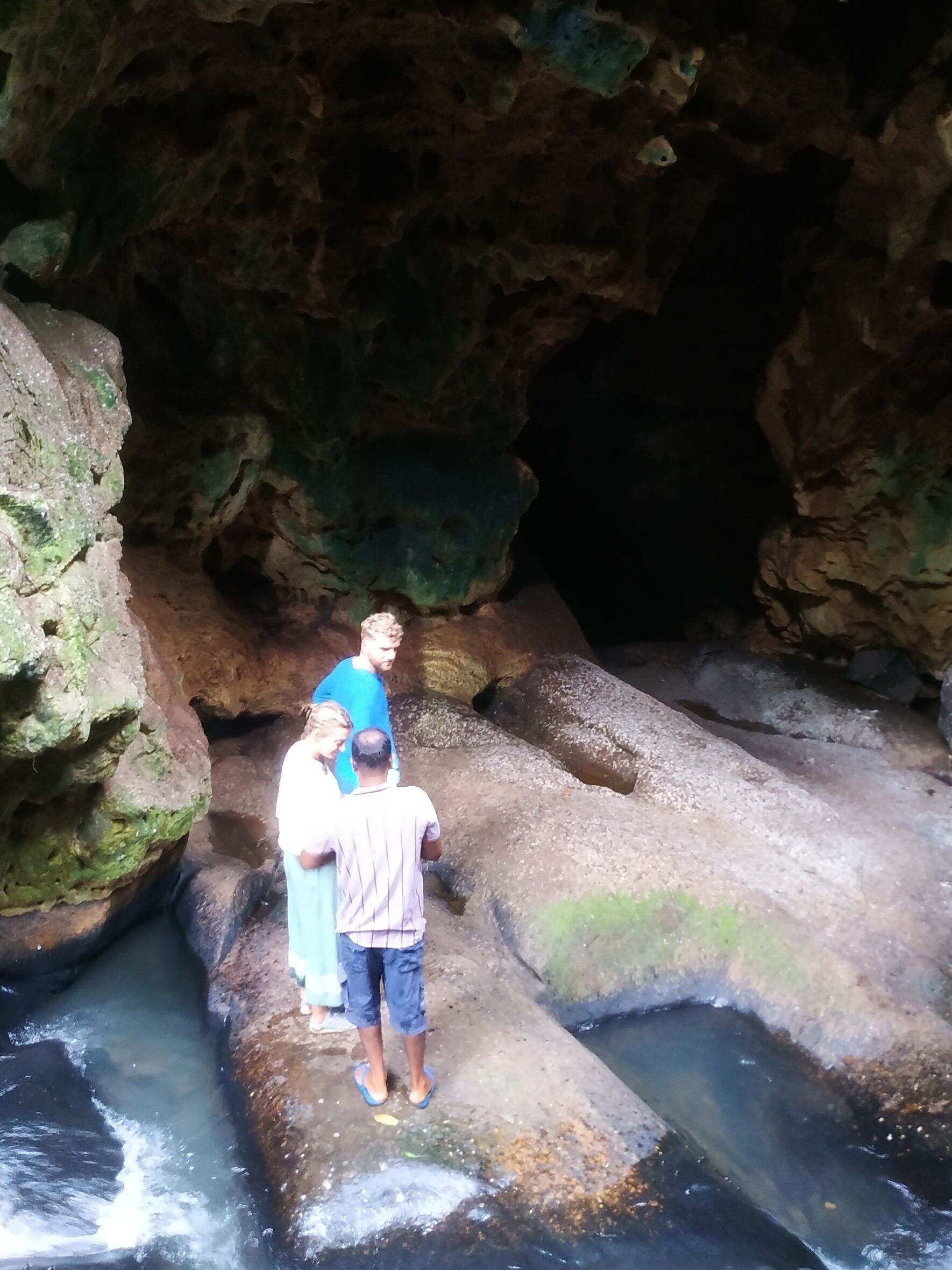 A group of people standing on a rocky ledge in a cave with water flowing below.