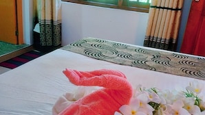 A neatly made bed with a pink towel and white flowers, a window with curtains, and a wooden door. - Greenwood Udawalawa safari resort (Udawalawa)