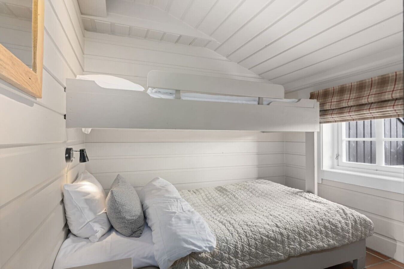 A bunk bed with a headboard, a bedside table, and a window with a plaid blind.