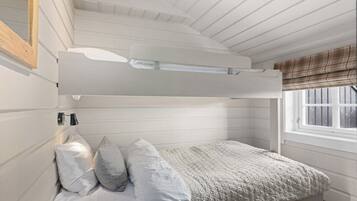 A bunk bed with a headboard, a bedside table, and a window with a plaid blind.