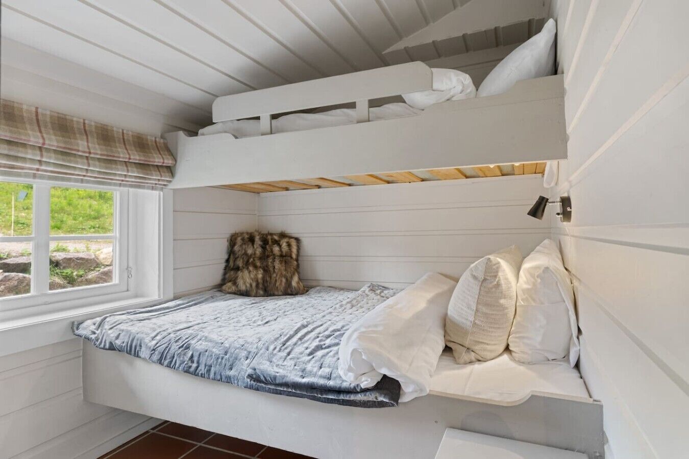 Een slaapkamer met stapelbed, raam, een bont tapijt en een wit hoofdeinde.