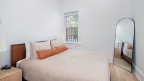 A bedroom with a large bed, a nightstand, a mirror, and a window with a view of greenery. - Stone Alley Condo 1 Bedroom Condo (Telluride)
