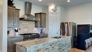 A modern kitchen with a central island, stainless steel appliances, and wooden cabinetry. - Casa Blanca | Waterfront, Pool + Pier (Rockport)