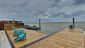 A wooden pier with turquoise Adirondack chairs and a small dock extending into calm water. - Casa Blanca | Waterfront, Pool + Pier (Rockport)