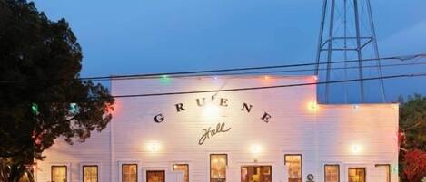 A white building with the name 'Gruene' on the facade, a water tower to the right, and cars parked in front.