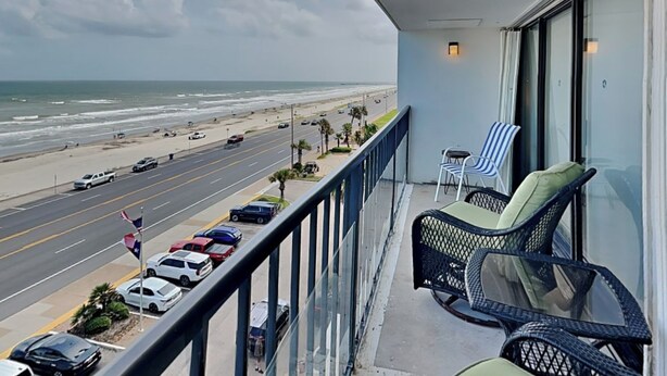 A balcony with a view of the beach and ocean, featuring two chairs and a table. - Sunny Sands | Cozy, Beachfront Condo (Galveston)
