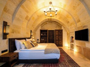 A bedroom with a large bed, a chandelier, a television mounted on the wall, and a fireplace. - Cybele in Cappadocia (Nevsehir)