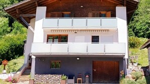 Un chalet de dos pisos con fachada de madera, un balcón en el nivel superior y un cimiento de piedra.