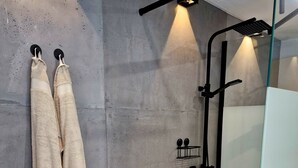 Un baño moderno con pared de concreto, cabina de ducha de vidrio y dos toallas colgadas en ganchos.