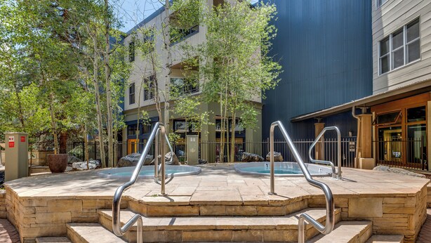 A stone staircase leading to a pool area with metal railings, surrounded by trees and buildings.