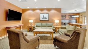 A modern living room with a flat-screen TV, a green sofa, a wooden coffee table, and brown armchairs.