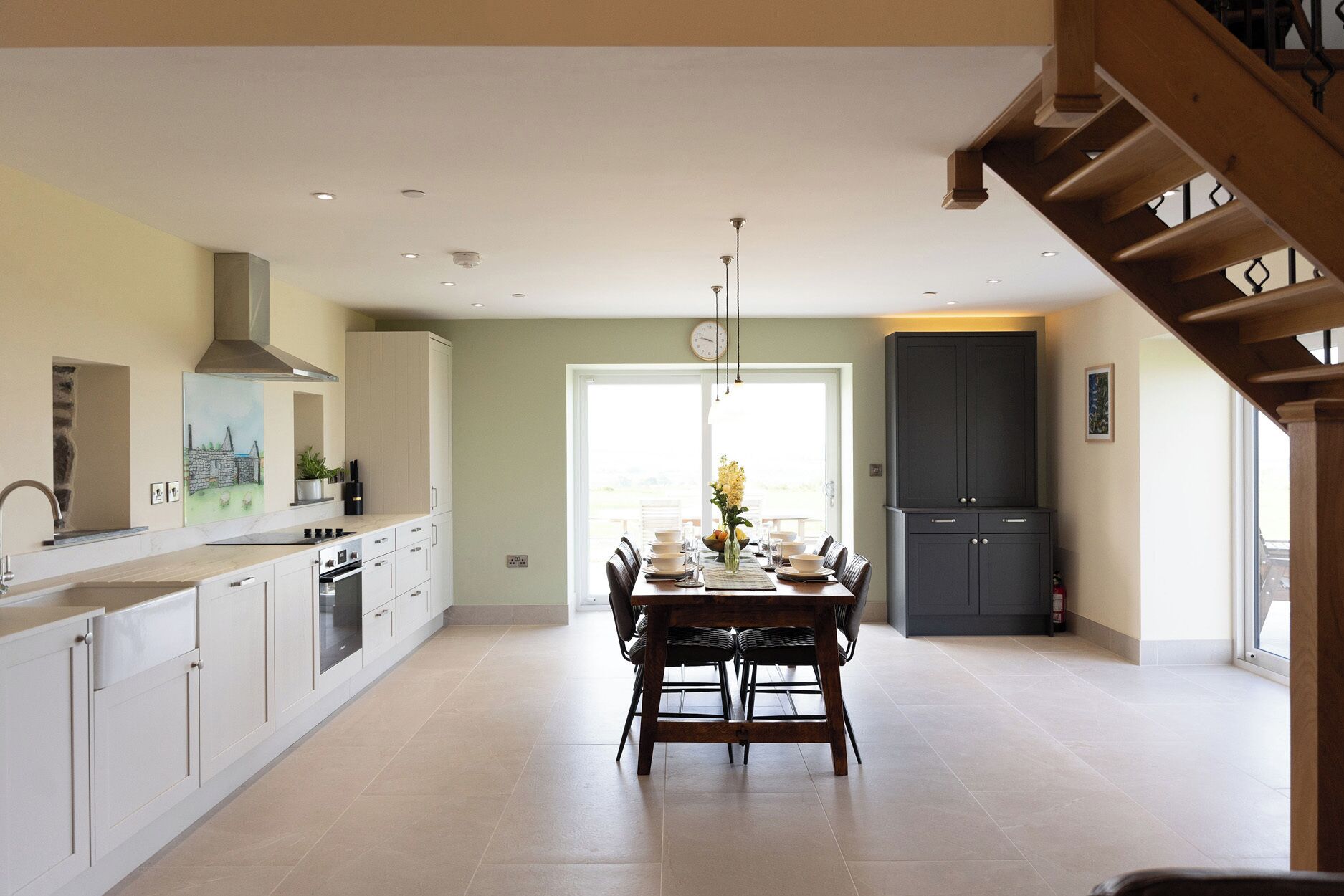 A spacious kitchen with a dining area, a staircase, and a view through a glass door.