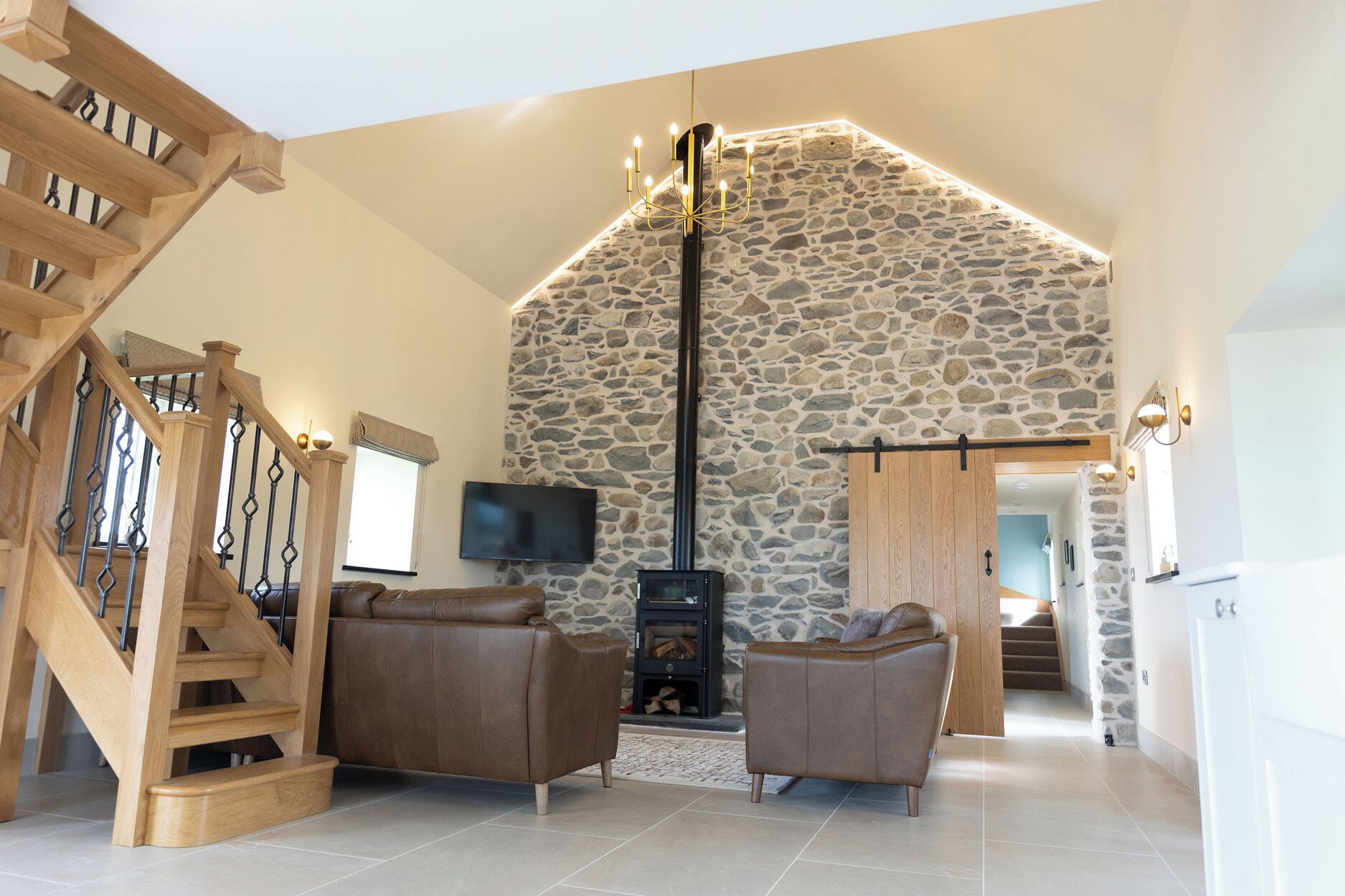 A spacious living area with a stone wall, a wooden staircase, and a fireplace.