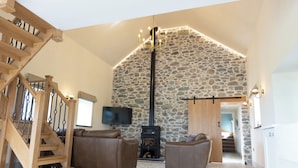 A spacious living area with a stone wall, a wooden staircase, and a fireplace. - Golygfa Cwrt (Talybont)