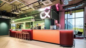 A modern bar area with a red counter, bar stools, and a large window providing a view of the city. - CX Modena Crocetta (Modena)