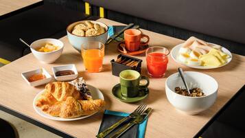 Una mesa de desayuno con cruasanes, fruta, jugo y café.