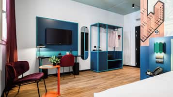 A modern hotel room with a wooden floor, a bed, a desk with a chair, a TV, a wardrobe, and a mirror.