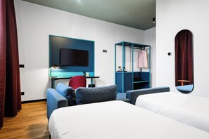 A modern hotel room with a bed, a desk, a chair, a TV, and a wardrobe.