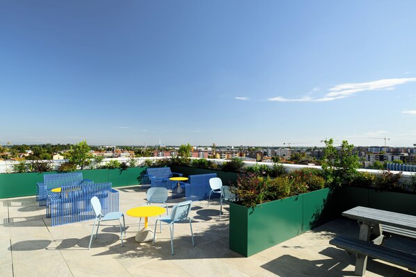 An outdoor seating area with blue and white chairs, a yellow table, and a green planter with flowers.