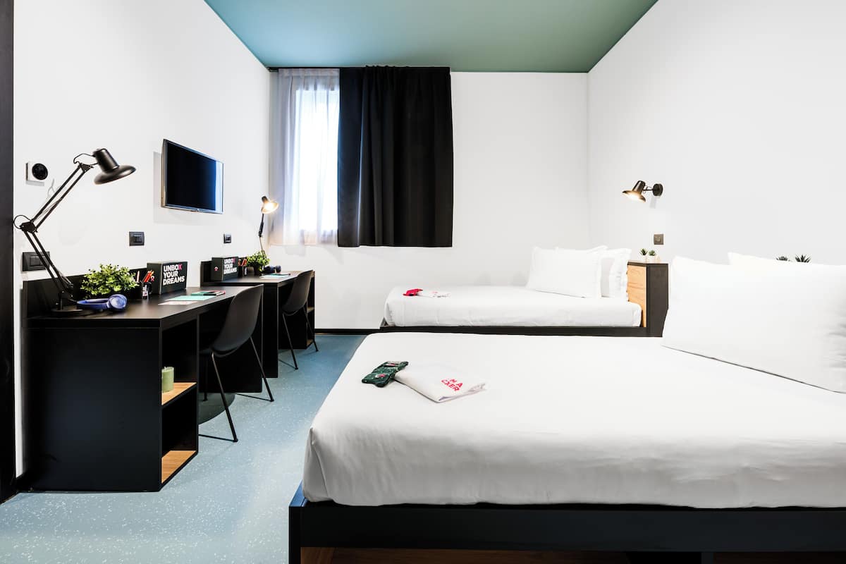 A hotel room with a desk, two beds, a TV, and a window with curtains.