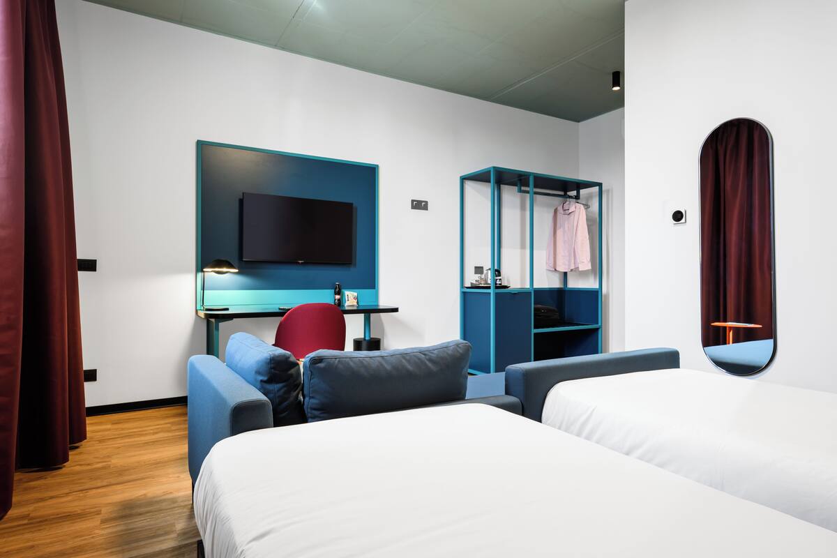 A modern hotel room with a bed, a desk, a chair, a TV, and a wardrobe.