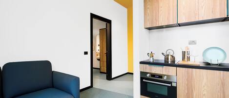 A modern kitchen with wooden cabinets, a black countertop, and a built-in oven. A blue sofa is positioned in the foreground.
