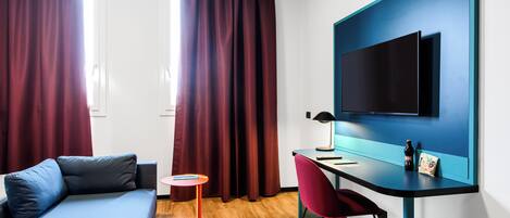 A modern hotel room with a bed, a desk, a chair, and a TV on the wall.