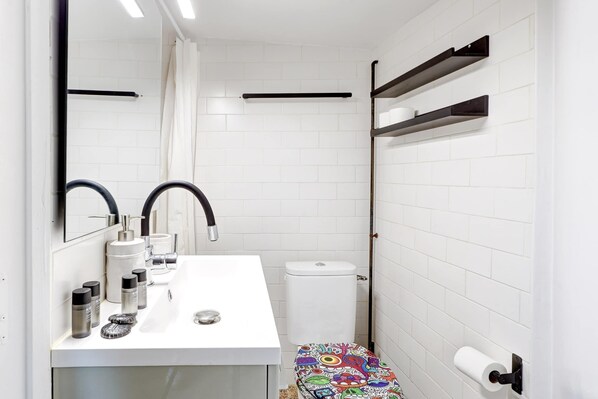 A compact bathroom with a white sink, two black faucets, a toilet, and a colorful bench. - Sous les toits de Montorgueil, vue magnifique (Paris)