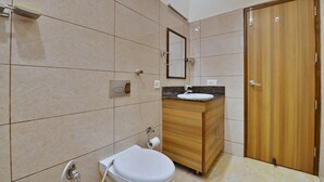A bathroom with a toilet, sink, mirror, and wooden door. - Hotel Aricent (Chandigarh)