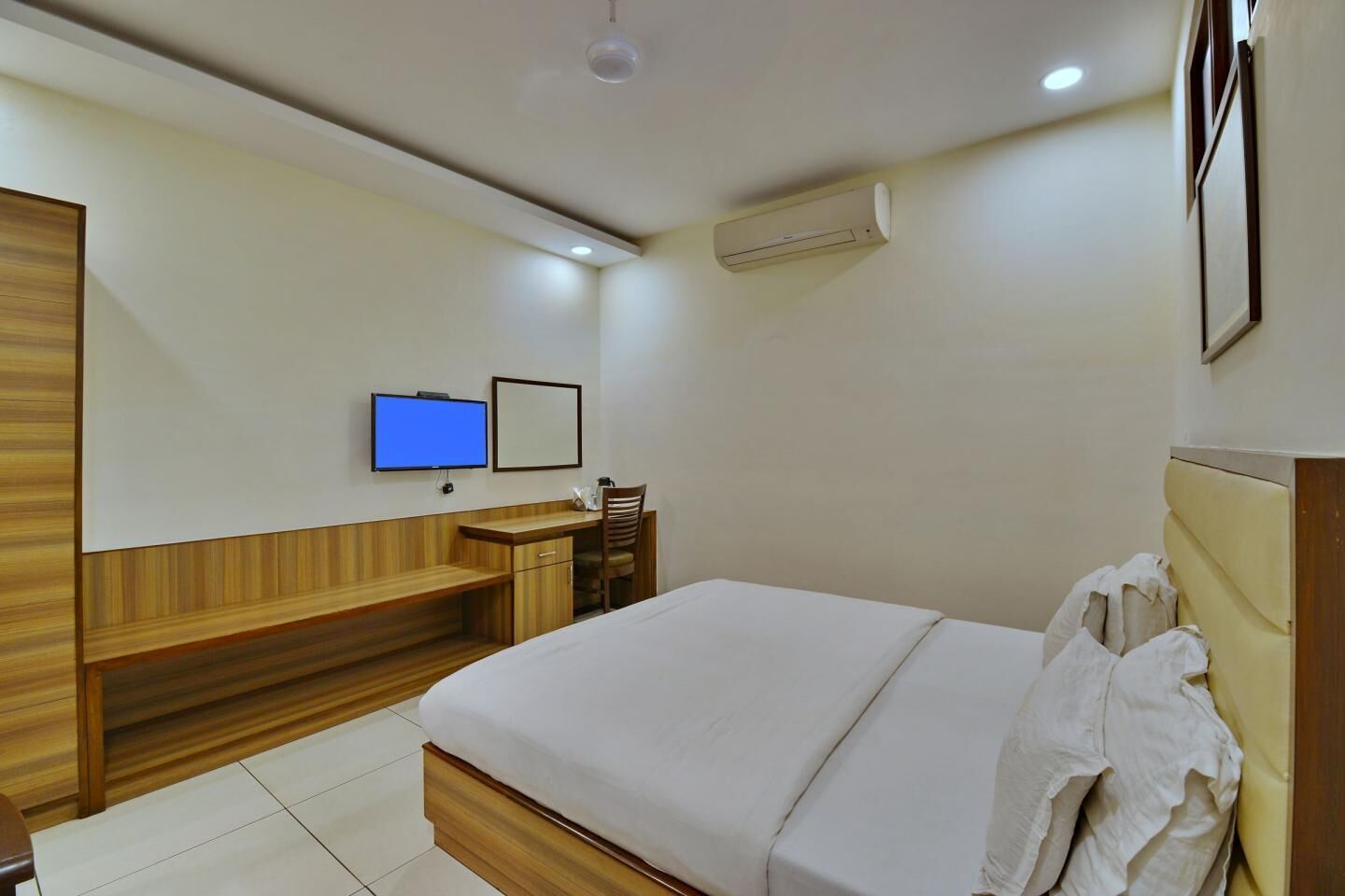 A hotel room with a bed, a desk, a chair, a television, and an air conditioning unit.
