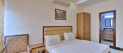 Habitación de hotel con cama, una silla, armario y baño visible a través de una puerta abierta.