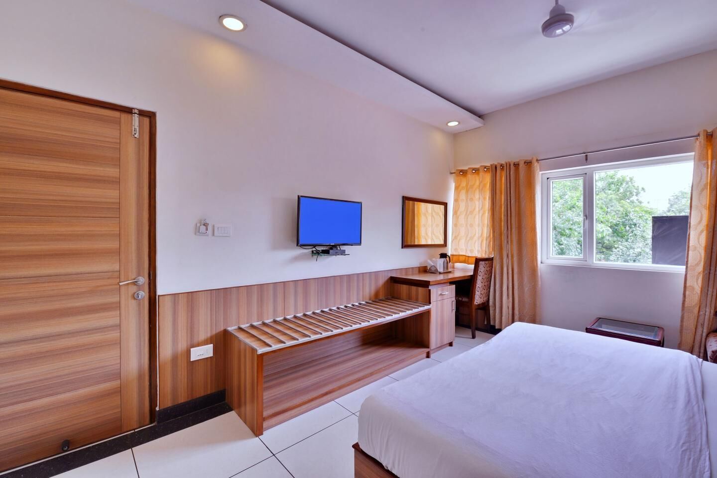 A hotel room with a bed, a desk, a chair, a television, and a window with curtains.