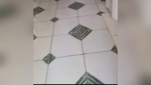 Een betegelde vloer met een geometrisch patroon, een witte muur en een houten plank met diverse spullen.