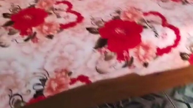 Een bed met een bloemenbedekking en een houten hoofdeinde.