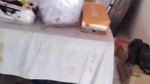 Een rommelige kamer met een bed, een tafel met een tafelkleed en verschillende schoenenparen.